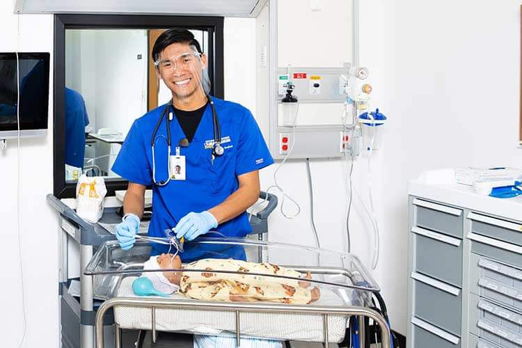 护理系的学生穿着蓝色的手术服站在旁边练习婴儿模型